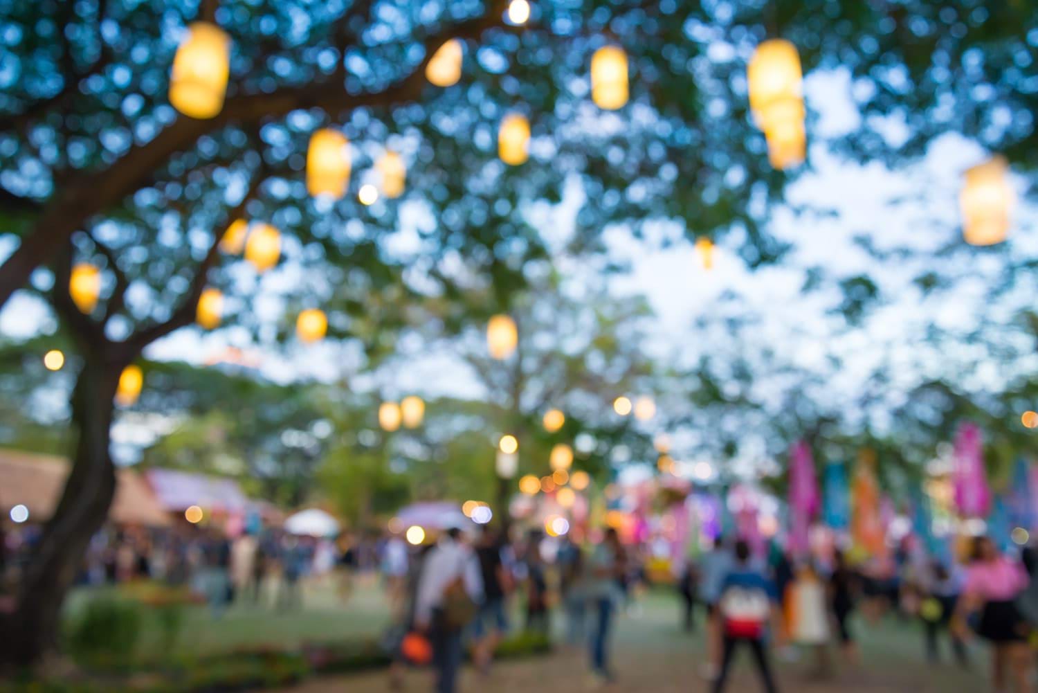 Lanterns hanging from a tree at dusk, with a crowd of people in the background