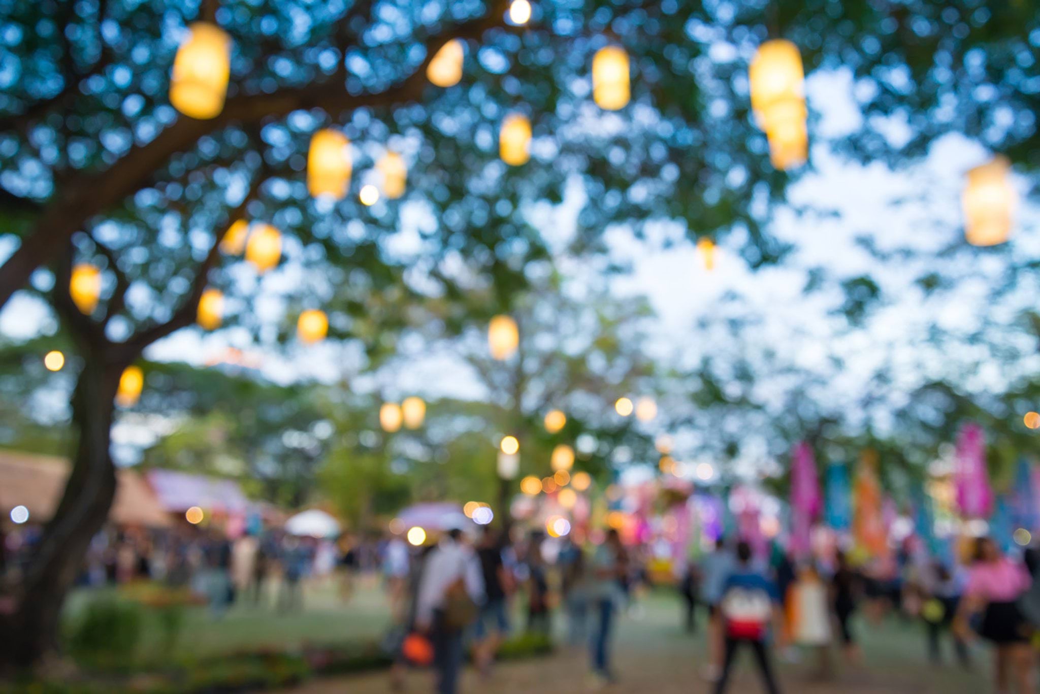 Lanterns hanging from a tree at dusk, with a crowd of people in the background